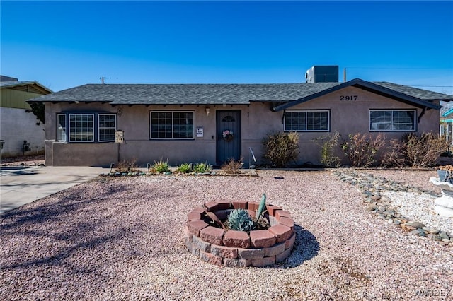 ranch-style house with a shingled roof, central AC, a fire pit, and stucco siding