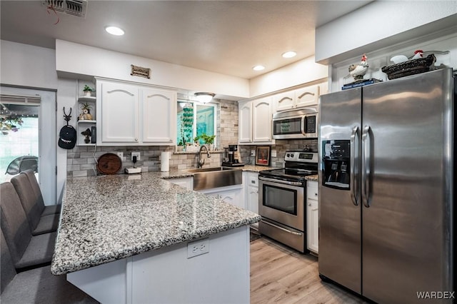 kitchen with appliances with stainless steel finishes, white cabinets, a sink, and a peninsula