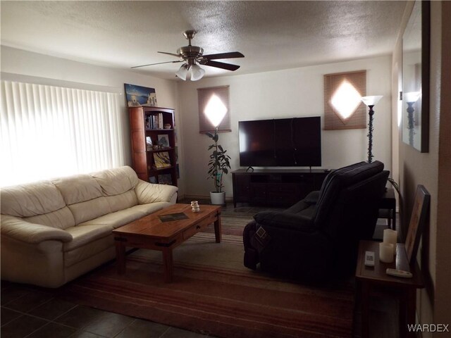 living room with ceiling fan, a textured ceiling, and dark tile patterned flooring