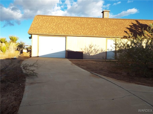 view of property exterior featuring a garage, a shingled roof, concrete driveway, and an outdoor structure