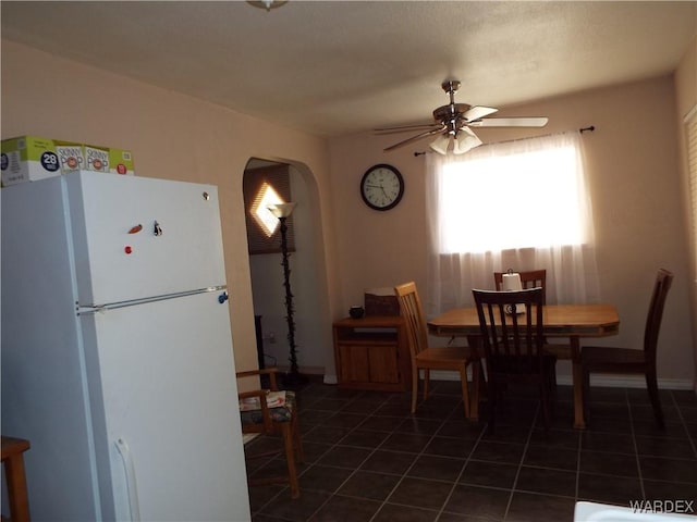 dining area featuring dark tile patterned floors, arched walkways, ceiling fan, and baseboards