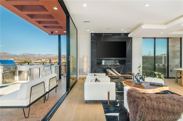 living room with a large fireplace, light wood finished floors, a wall of windows, and recessed lighting