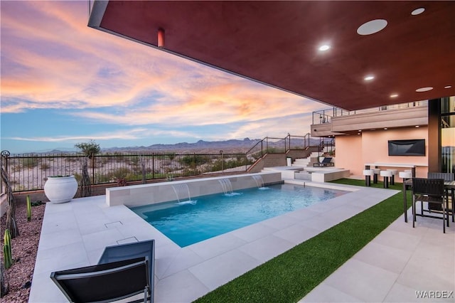 pool at dusk featuring a fenced in pool, a patio area, a mountain view, and fence