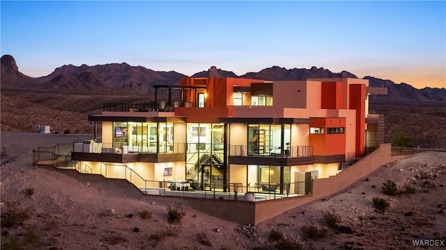 back of property at dusk featuring a mountain view and stucco siding