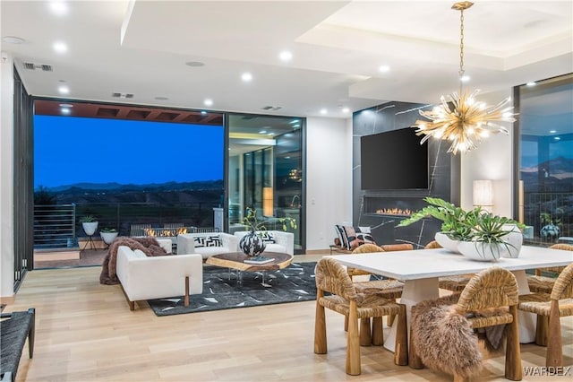 dining room featuring light wood finished floors, visible vents, expansive windows, a fireplace, and a notable chandelier