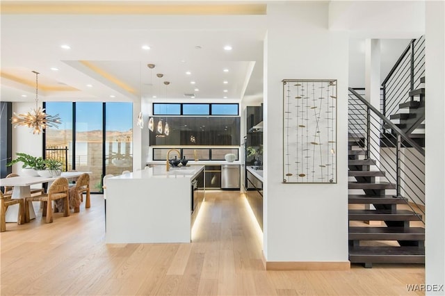 kitchen with pendant lighting, light countertops, light wood-style floors, a kitchen island with sink, and a sink