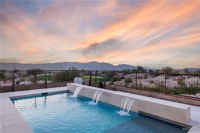 pool at dusk featuring fence, a mountain view, and a fenced in pool