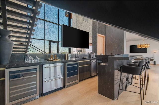 bar featuring wine cooler, a notable chandelier, light wood-style flooring, and wet bar