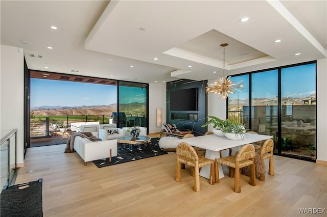 dining space featuring a tray ceiling, floor to ceiling windows, recessed lighting, an inviting chandelier, and light wood-type flooring