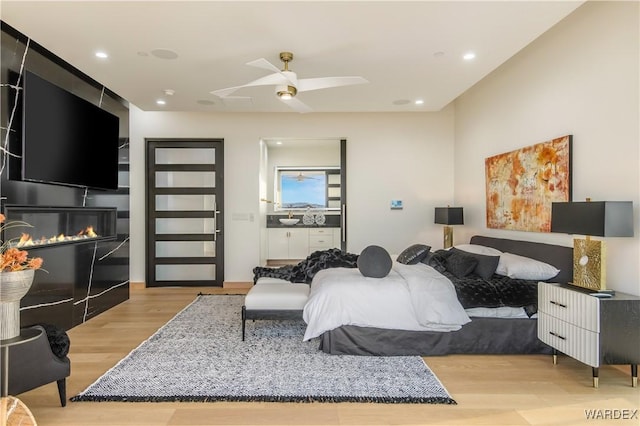 bedroom featuring recessed lighting, light wood-style flooring, a ceiling fan, and a glass covered fireplace