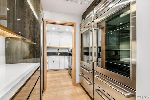 kitchen with light wood finished floors, double oven, modern cabinets, and white cabinets