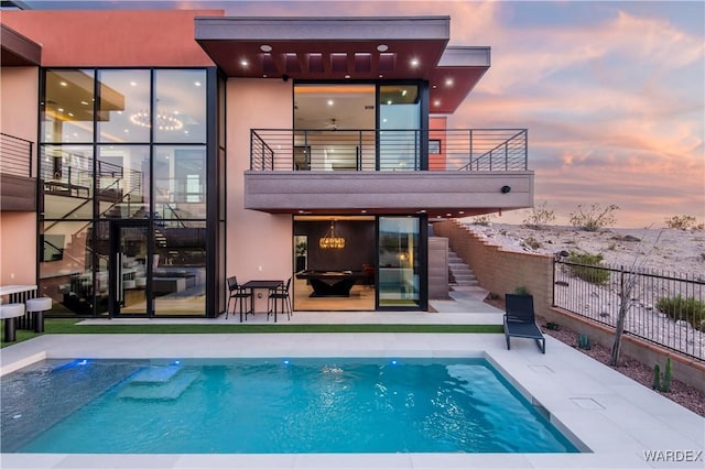 back of house featuring a fenced in pool, fence, a balcony, and stucco siding