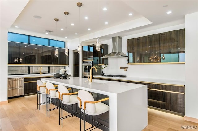 kitchen featuring light countertops, wall chimney range hood, modern cabinets, and a center island with sink