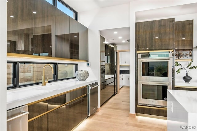 kitchen with stainless steel appliances, a sink, light countertops, light wood-type flooring, and modern cabinets