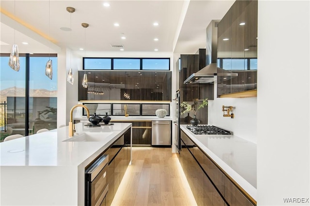 kitchen featuring light countertops, hanging light fixtures, a sink, island range hood, and modern cabinets