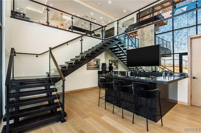 bar with a high ceiling, light wood finished floors, wet bar, and stairway