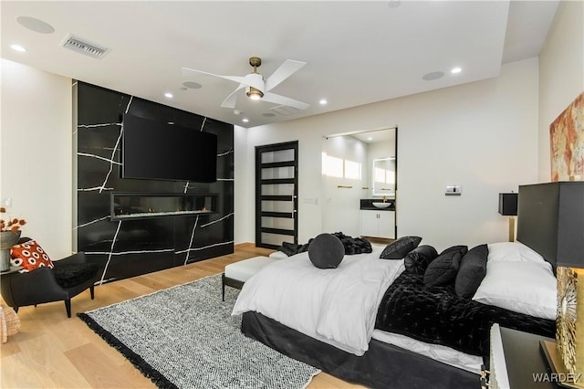 bedroom featuring recessed lighting, a ceiling fan, visible vents, light wood finished floors, and a glass covered fireplace