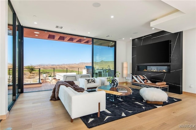 living room featuring a large fireplace, light wood-style floors, visible vents, and floor to ceiling windows