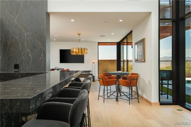 bar featuring hanging light fixtures, light wood-style floors, plenty of natural light, and a wall of windows