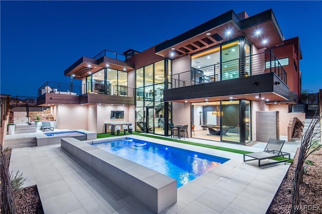 back of house at twilight with a patio, stucco siding, a balcony, a jacuzzi, and an outdoor pool