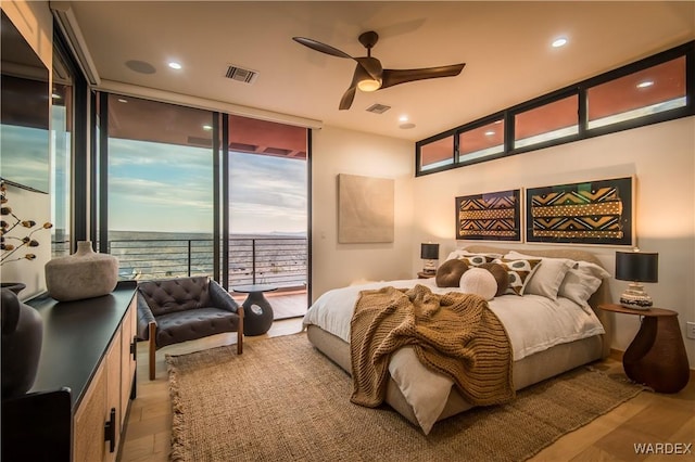 bedroom featuring a water view, light wood-type flooring, access to outside, and floor to ceiling windows