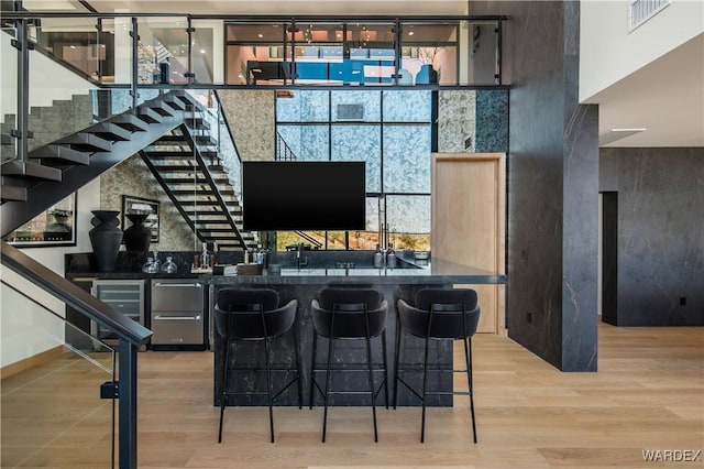 bar with light wood-type flooring, indoor wet bar, stairway, and a high ceiling