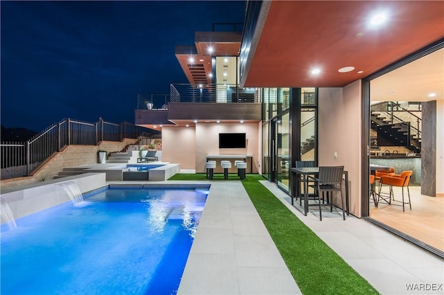 pool at night with a patio area, fence, and a fenced in pool