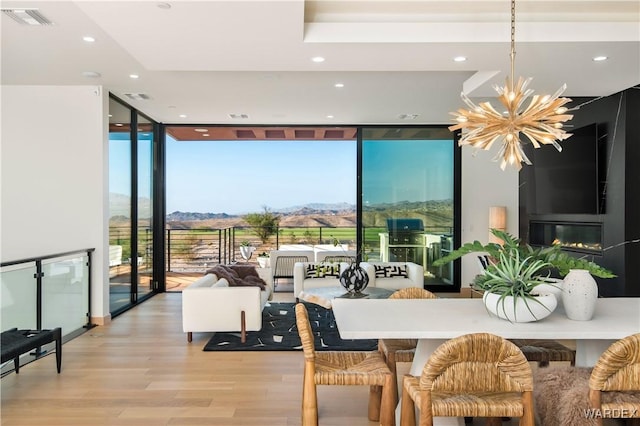 dining space with an inviting chandelier, visible vents, a wall of windows, and light wood-style floors