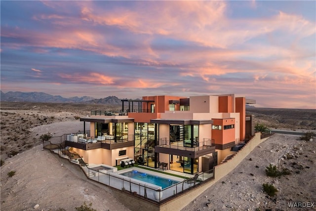 back of house featuring an in ground hot tub, a mountain view, and stucco siding