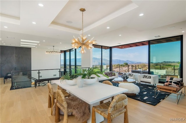 dining space featuring floor to ceiling windows, a notable chandelier, light wood finished floors, a raised ceiling, and a mountain view