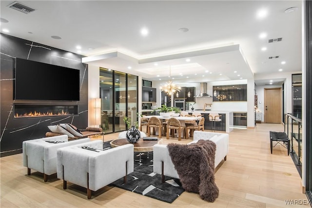 living area with light wood finished floors, a fireplace, visible vents, and a notable chandelier