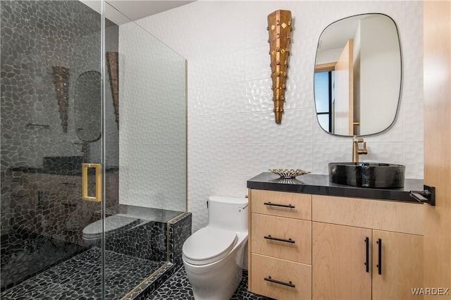 full bathroom with a shower stall, tile walls, toilet, and vanity