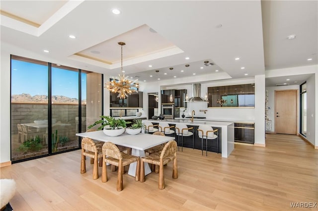 dining space with recessed lighting, expansive windows, light wood finished floors, a raised ceiling, and an inviting chandelier