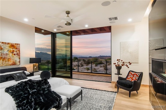 bedroom with access to exterior, floor to ceiling windows, a fireplace, visible vents, and wood finished floors