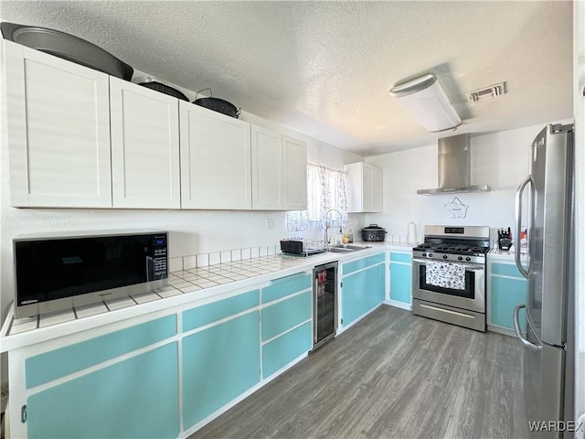 kitchen with tile countertops, beverage cooler, stainless steel appliances, white cabinets, and wall chimney exhaust hood