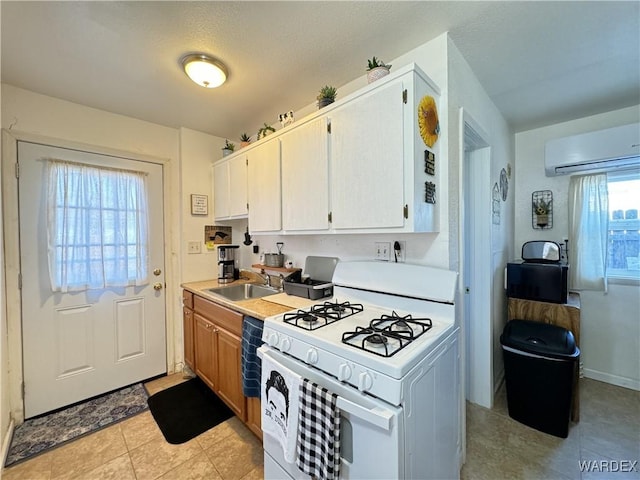 kitchen featuring white range with gas stovetop, light countertops, white cabinetry, a sink, and a wall mounted AC