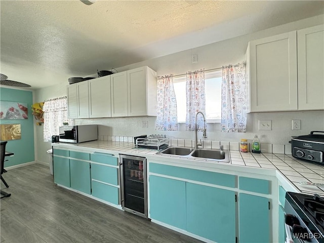 kitchen featuring tile countertops, appliances with stainless steel finishes, white cabinets, a sink, and beverage cooler