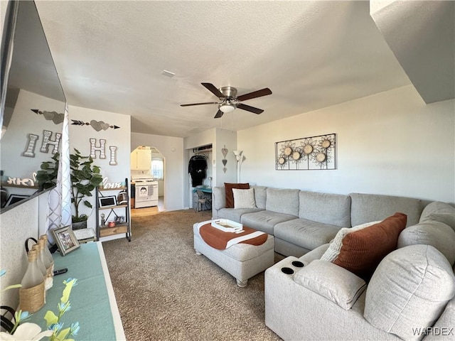 living room with carpet floors, a textured ceiling, arched walkways, and a ceiling fan