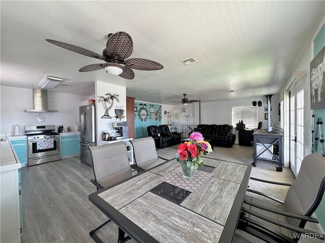 dining room featuring light wood-type flooring, a ceiling fan, visible vents, and a textured ceiling