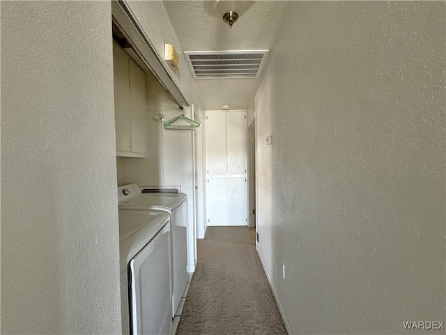 washroom with a textured wall, visible vents, independent washer and dryer, cabinet space, and carpet