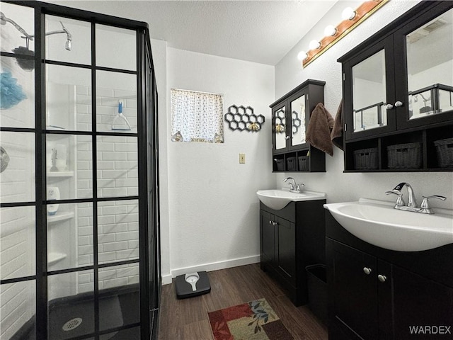 full bath with a stall shower, two vanities, a sink, and wood finished floors