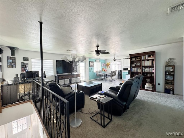 living room featuring ceiling fan, a textured ceiling, carpet flooring, and visible vents