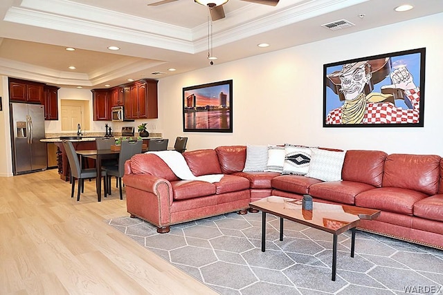 living room with a tray ceiling, crown molding, light wood-style flooring, and recessed lighting