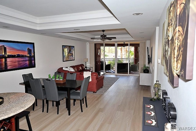 dining area featuring light wood-type flooring, a tray ceiling, a ceiling fan, and ornamental molding