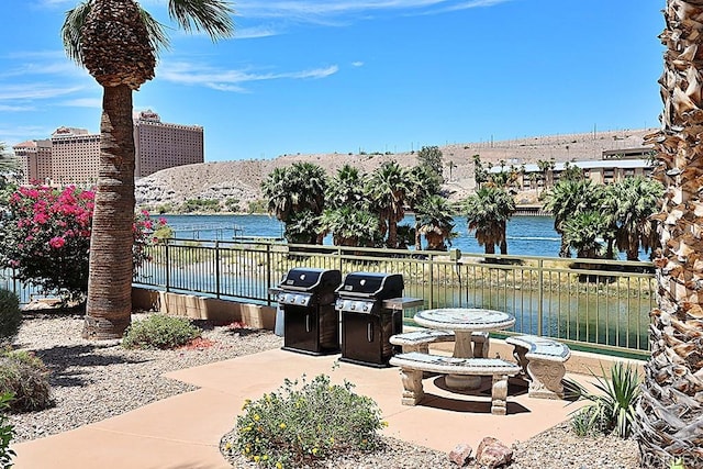 view of patio with area for grilling, a water view, and fence