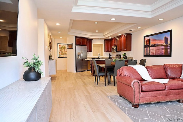 living room featuring a tray ceiling, crown molding, light wood finished floors, recessed lighting, and baseboards