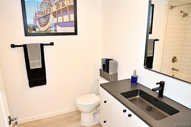 full bathroom with baseboards, toilet, wood finished floors, vanity, and washtub / shower combination