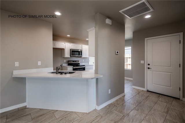 kitchen featuring appliances with stainless steel finishes, a sink, white cabinets, baseboards, and a peninsula