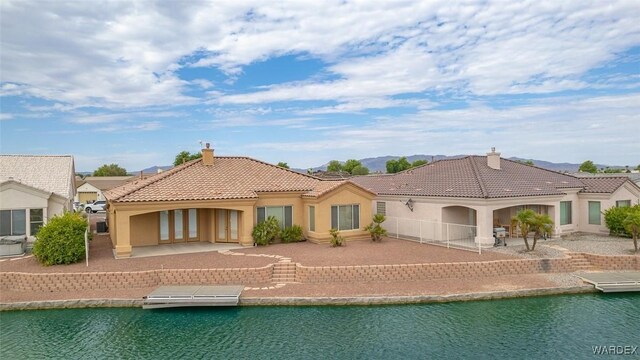 back of house featuring a patio, a chimney, stucco siding, a water view, and a tiled roof