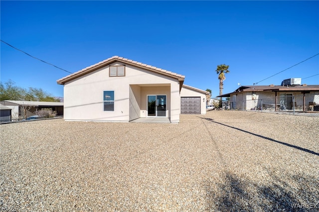 rear view of property with a tile roof, an attached garage, and stucco siding